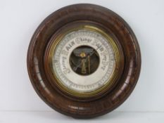 An Edwardian aneroid barometer in decorative circular wooden frame, 22cm dia, glass deficient.