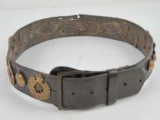 A leather belt with various cap badges and buttons attached.