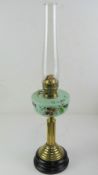 A brass oil lamp handing hand painted opaque green glass reservoir, with chimney.