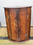 A late Georgian barrel fronted hanging corner cabinet in mahogany and walnut, two shelves within,