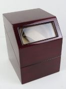 An electrically operated watch winder, glazed mahogany effect cabinet, with charger, 13cm wide.