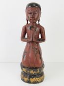 A painted wooden carving of a praying figure, 41cm high.