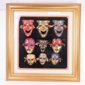 A montage of nine enamelled brass decorative masks mounted on black velvet with gold painted frame