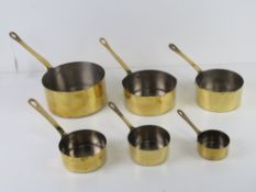 A set of six graduated brass saucepan.