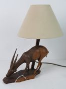 A carved wooden table lamp in the form of an African Gazelle type animal, slight a/f, with shade.