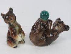 A pair of ceramic bear figurines, one playing with green ball, one marked to base CW39.