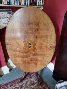 An oval tilt top half veneered walnut table raised over quatreform base, 118 x 87cm.