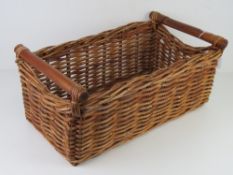 A wicker basket with wooden end handles.