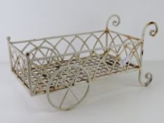 A white painted metal planter in the form of a wheelbarrow, 46cm in length.