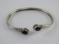 A silver and amethyst bangle, stamped 925 and having oval cabachon to each terminal.