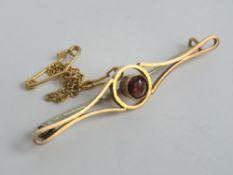 An Edwardian yellow metal bar brooch having central burgundy coloured stone, with safety chain/pin,