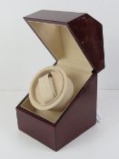 An electrically operated watch winder, glazed mahogany effect cabinet, with charger, 13cm wide.