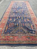 An early 20thC red and blue ground rug having geometric design of trees upon, 5 x 2.25m.