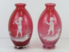 A pair of cranberry glass Mary Gregory type bud vases, each standing 14.5cm high.