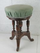 A Victorian piano stool raised over triform base and upholstered in green fabric.