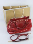 Michael Kors; a red patent handbag with original paper shopping bag and dust bag, approx 31cm wide.