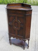 A c1930s Arts & Crafts floor standing oak corner cupboard having panel door opening to reveal