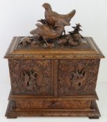 An impressive 19thC black forest carved tabletop cabinet having pair of partridges with chicks upon,