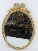 An oval mirror having ribbon type gilt frame, 55.5cm high.