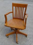 A pine Captain's type office chair raised over brass capped castors.