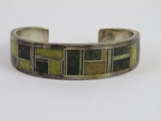 A Native American sterling silver bangle set with green hardstones in geometric pattern,
