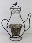 A teashop sign having wicker planter within black metal 'teapot' frame with Welcome sign over,