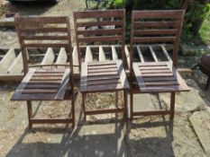 A set of three wooden folding garden chairs.