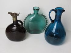 Three assorted coloured glass claret jugs, one having metal lid and cover,