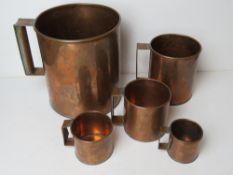 A set of five graduated copper measuring cups being gallon, quart, pint, half pint and gill.