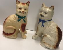Two pottery cats, one wearing a green bo