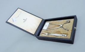 A boxed Georg Jensen silver sugar tongs and lemon fork, circa 1920. The box 10 cm wide. 38 grammes.