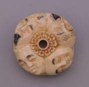 A bone toggle carved with faces. 4 cm diameter.