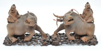 A pair of Chinese carved wooden water buffalo with figural riders and glass eyes, on rosewood