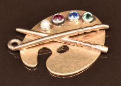 A 9ct gold c1920 pendant or charm in the form of a artist's palette and brushes, set with a seed