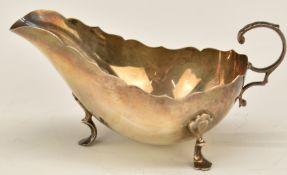 George VI hallmarked silver sauce boat with shaped edge and scrolling handle, raised on three