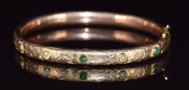 A 9ct gold bangle set with emeralds and diamonds with engraved floral decoration, 14.7g, 6.2 x 5.