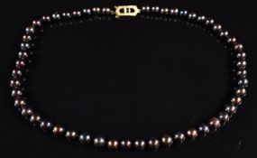 A single strand of black pearls, the yellow metal clasp set with a garnet, 40cm long, 24.7g