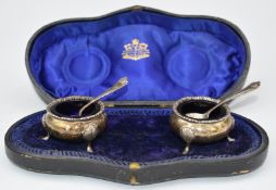 Cased pair of George V hallmarked silver salts, raised on three feet, with blue glass liners and