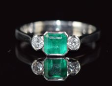A platinum ring set with an octagonal emerald of approximately 0.65ct and two diamonds, each