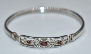 A silver bangle set with three garnets in a pierced setting, 6 x 5cm