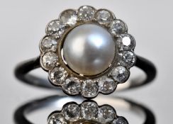 A c1910 platinum ring set with a natural pearl measuring approximately 6.8mm surrounded by diamonds,