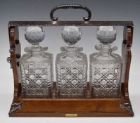 Betjamann's Patent oak and silver plated three bottle tantalus with cut glass bottles and Bramah