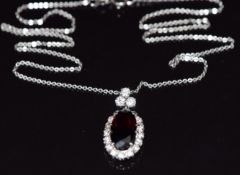 An 18ct white gold pendant set with an oval cut garnet surrounded by diamonds, with three additional
