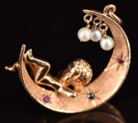 A 14k gold pendant in the form of a cherub sitting on the moon, set with pearls, rubies and