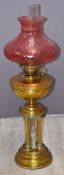 Victorian figural oil lamp with Corinthian column supports and cranberry glass shade, height 83cm