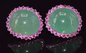 A pair of white gold earrings set with a large jadeite cabochon surrounded by 26 rubies each