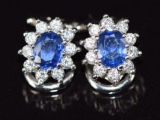 A pair of 18ct white gold earrings, each set with a natural oval cut sapphire surrounded by ten