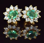 A pair of 18k gold earrings each set with an oval cut emerald of approximately 0.4ct surrounded by