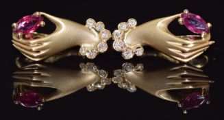 A pair of 14k gold earrings each in the form of a hand holding a marquise cut ruby, with diamonds to