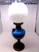 An antique brass oil lamp with blue glass reservoir, chimney and opaque glass shade,